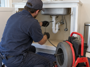 Plumber using drain cleaning equipment beneath a kitchen sink